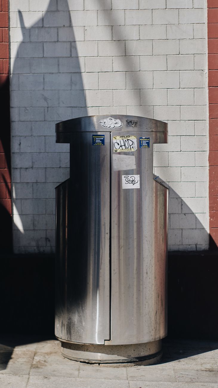 silver trash bin beside white wall